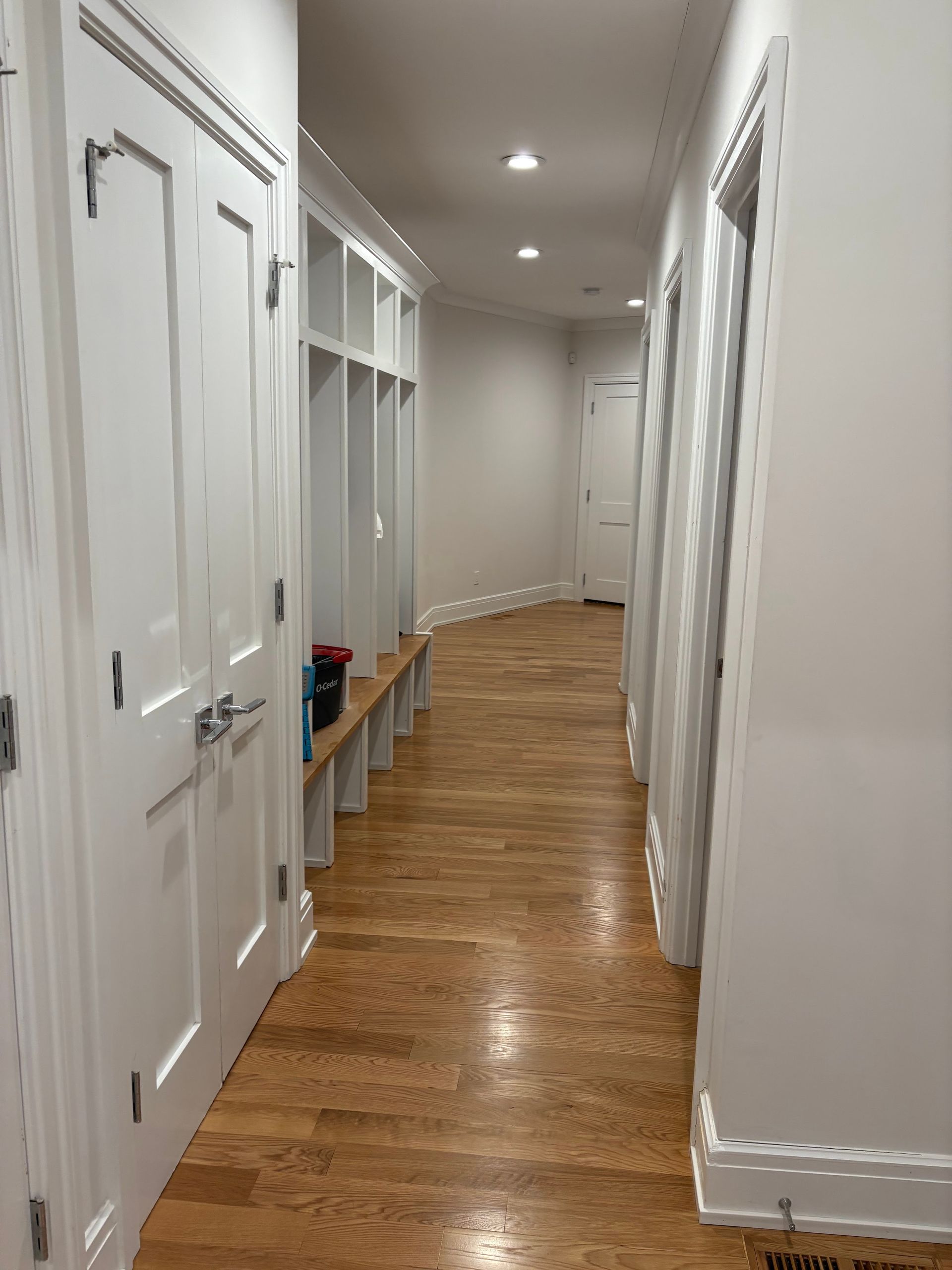 Bright hallway with white doors, built-in shelves, and polished wood floors leading to a distant end.