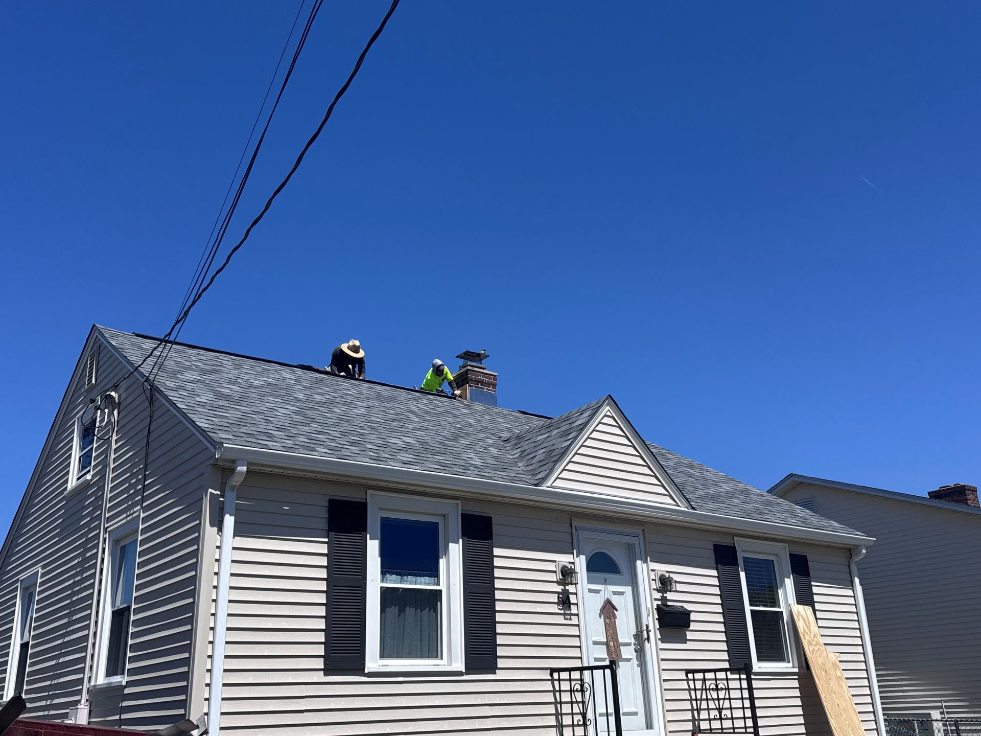 Workers repairing a gray house roof under a bright blue sky