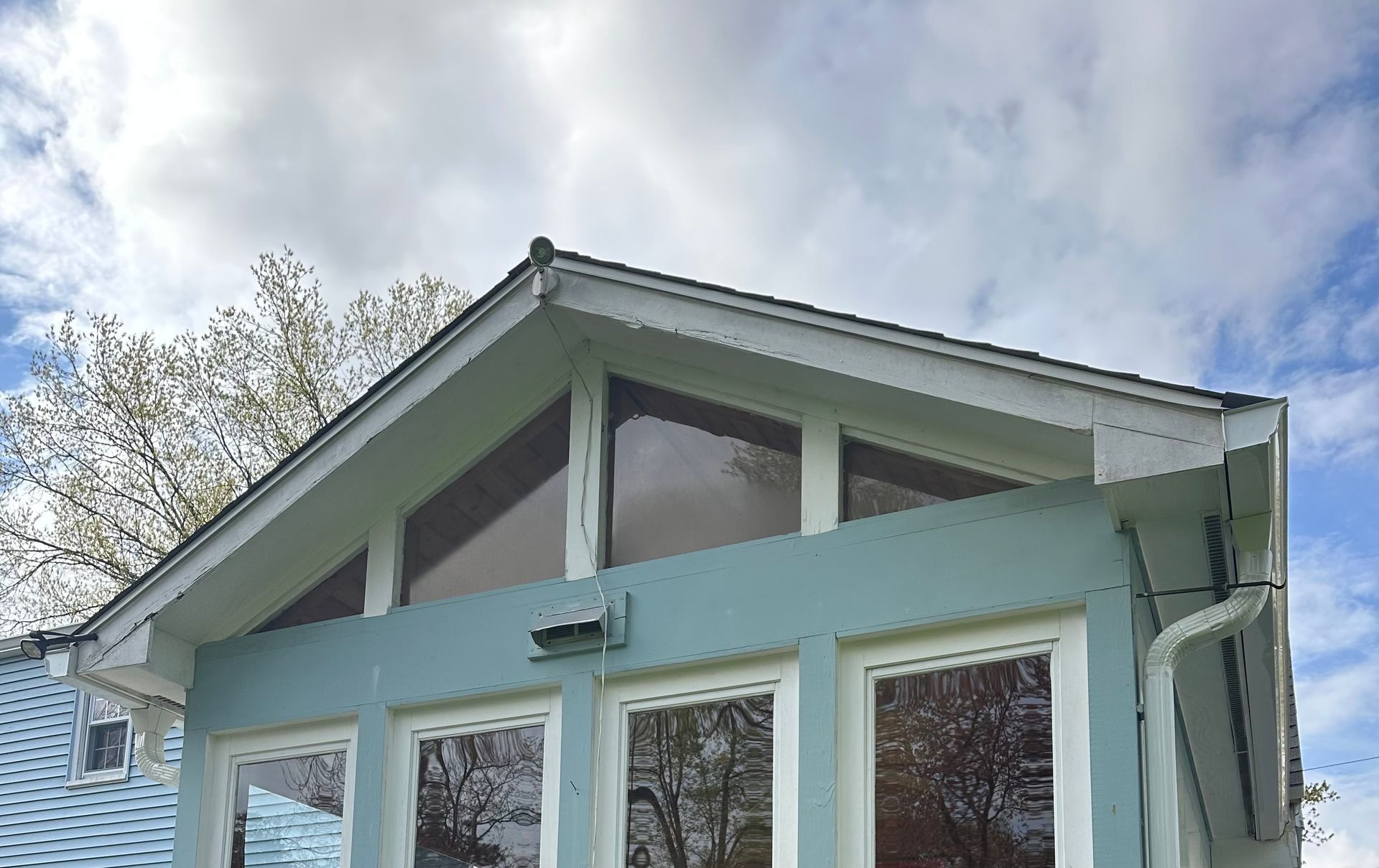 Light blue house facade with large windows and a peaked roof against a cloudy sky