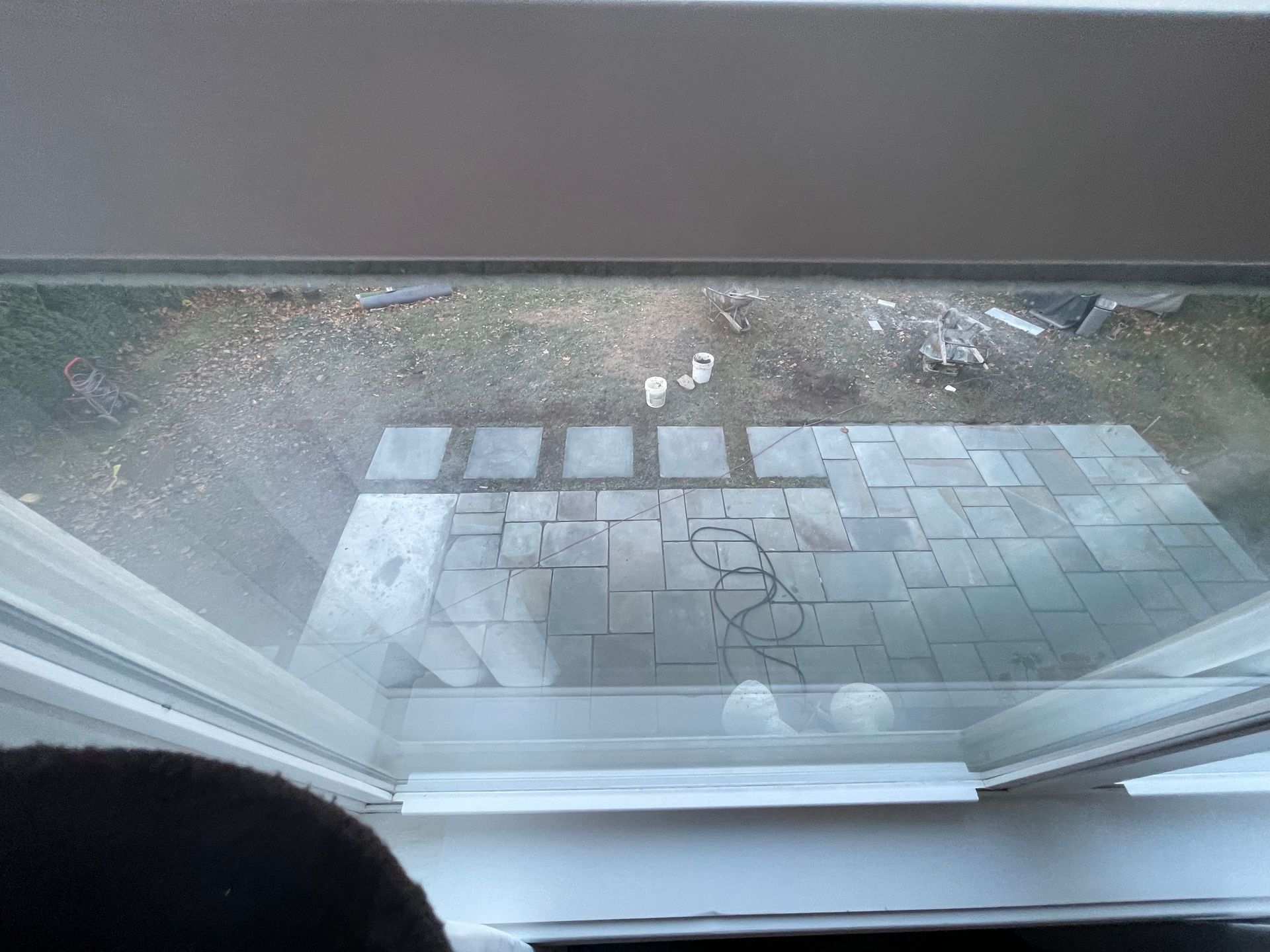 View through a window onto a wet stone patio with scattered leaves and small white objects.