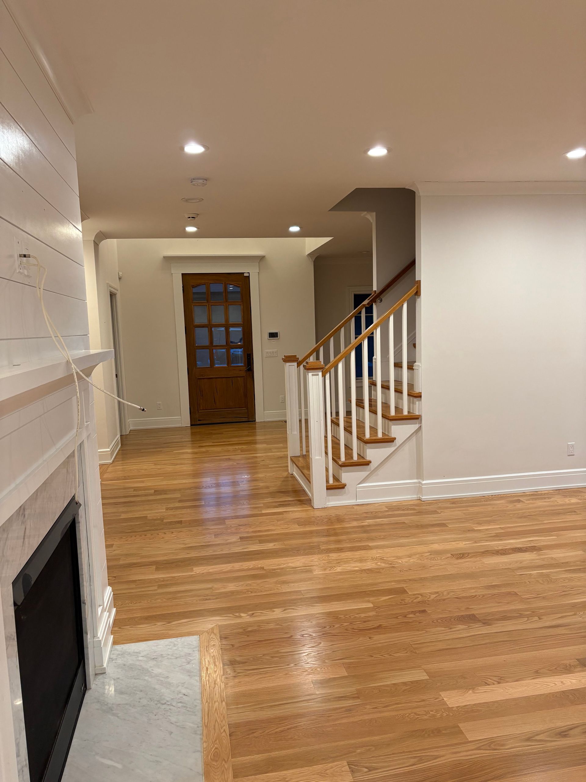 Empty living room with hardwood floors, fireplace, and staircase leading to a wood front door