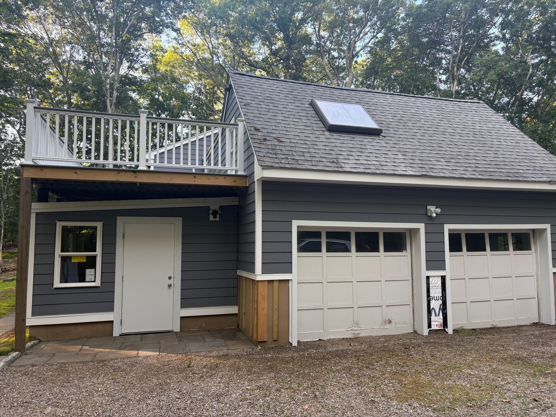 Gray house with rooftop deck, white door, and double garage beneath a shingled roof