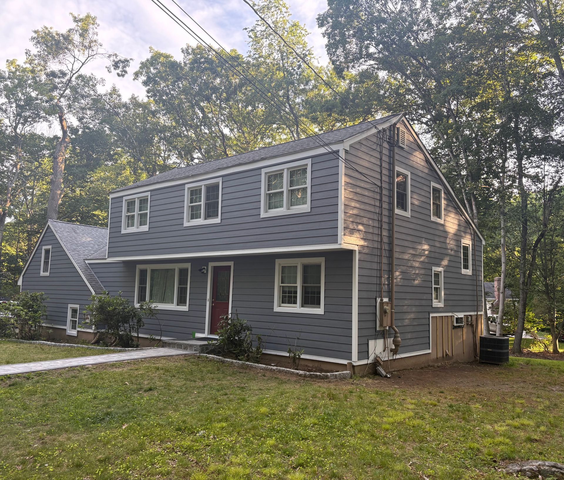 Gray two-story house with white trim and a red door, surrounded by trees and a grassy yard.