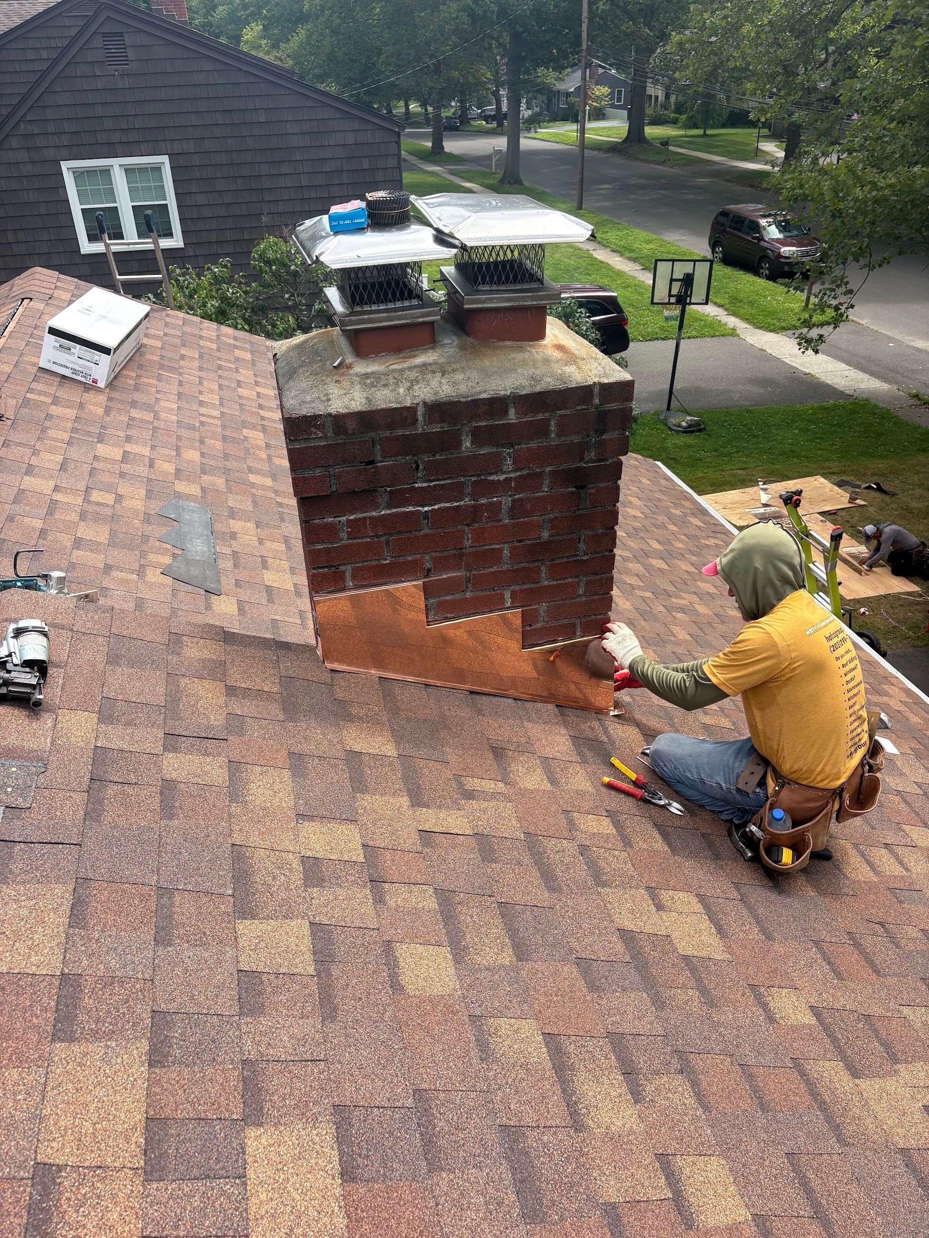 Worker repairing a brick chimney on a shingled roof in a residential neighborhood