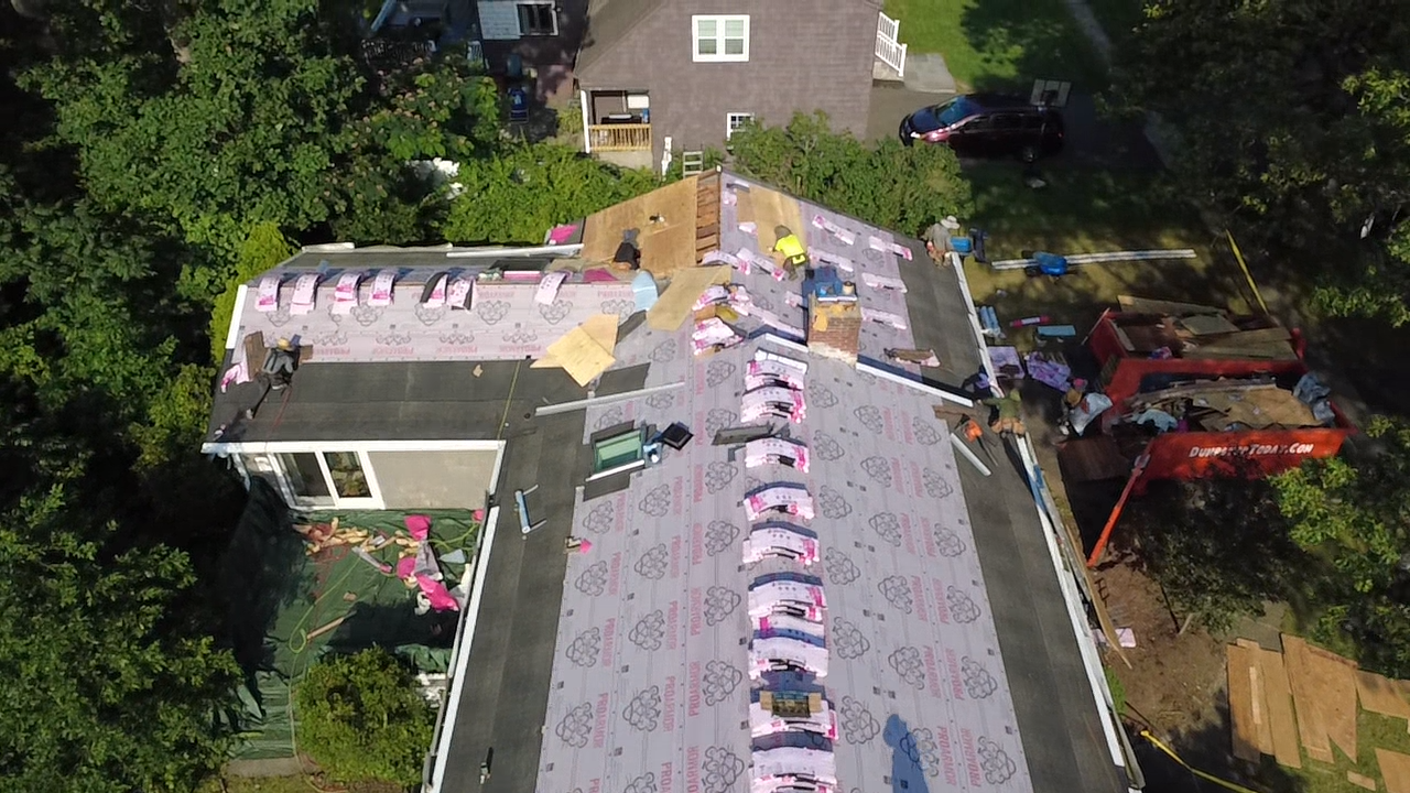 Aerial view of a rooftop with rows of pink and white decorations beside a house and trees