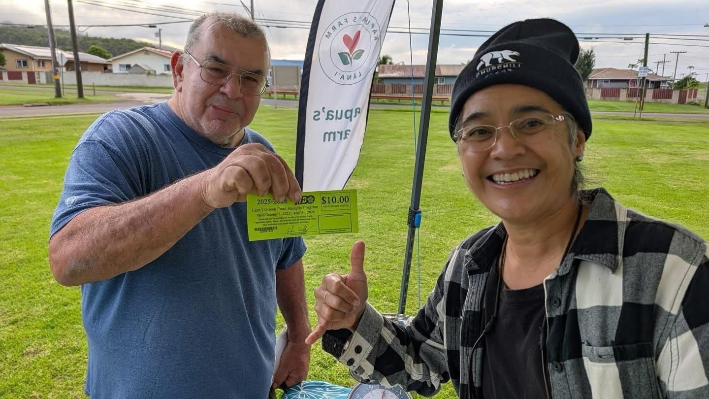Two smiling people holding a flag at a grassy outdoor event.