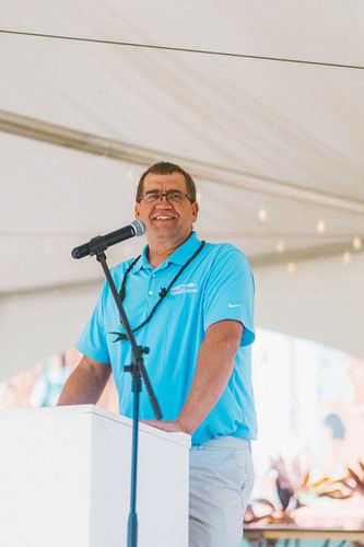 Man in a light blue shirt speaking at a podium under a white tent