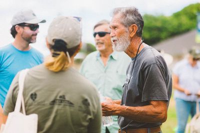 Small outdoor group chatting, with an older man in a gray shirt speaking in the foreground.