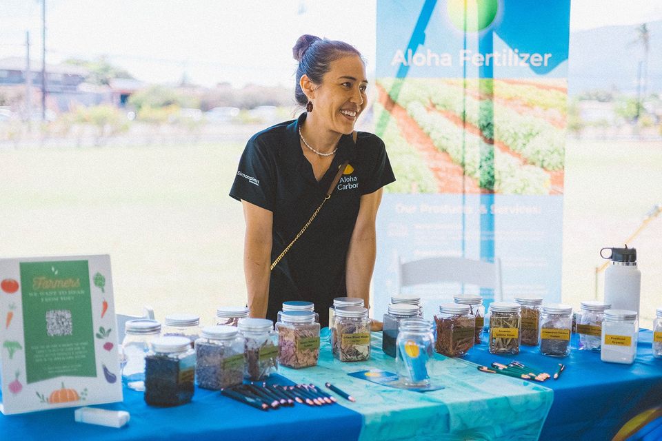 Woman smiling behind a table of jars and containers at an outdoor market stall
