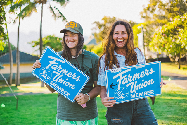 Two people holding blue Farmer's Union member signs in a sunny park