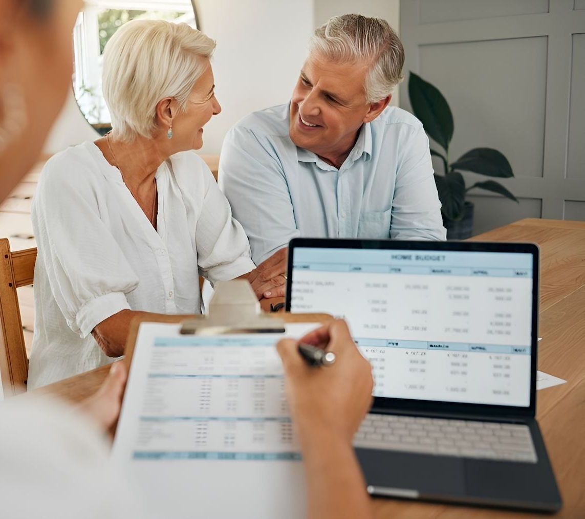 A Man And A Woman Are Sitting At A Table Looking At A Laptop — Loretta Davison Financial Solutions In Austinmer, NSW