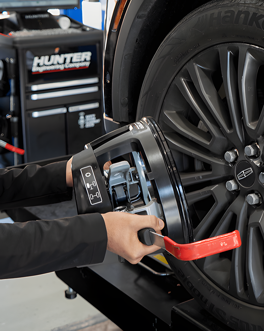 Person using wheel alignment equipment on a car tire in a shop setting.