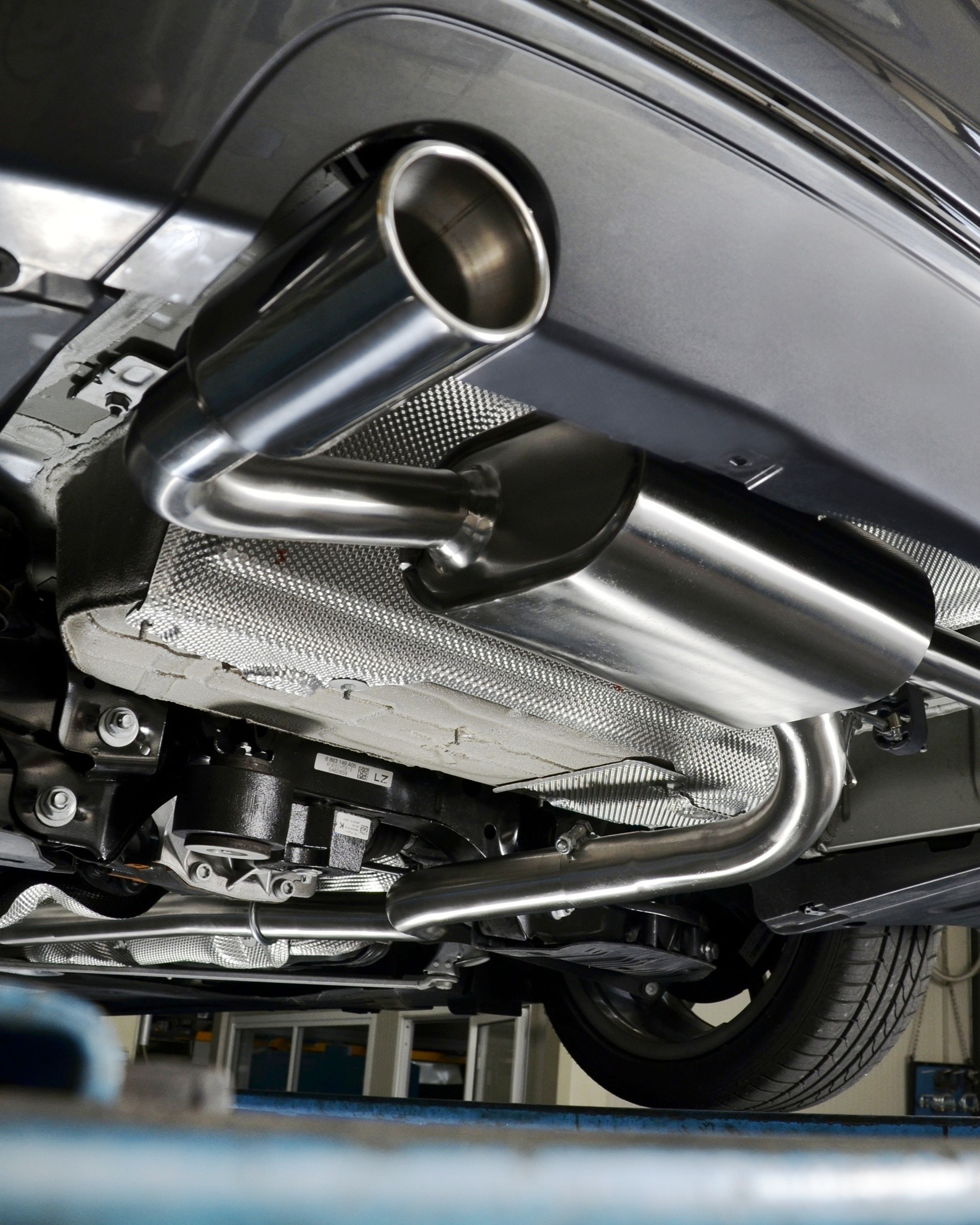 Underside of a car showing a shiny exhaust system, including a muffler and dual chrome tailpipes.