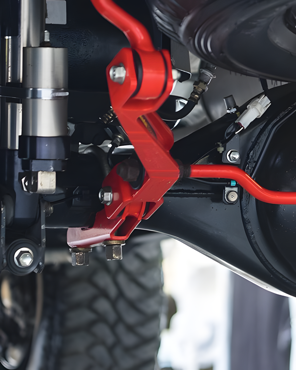 Red sway bar links on a vehicle's undercarriage, attached to the axle and suspension components.