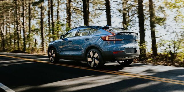 Blue Volvo C40 driving on a tree-lined road.