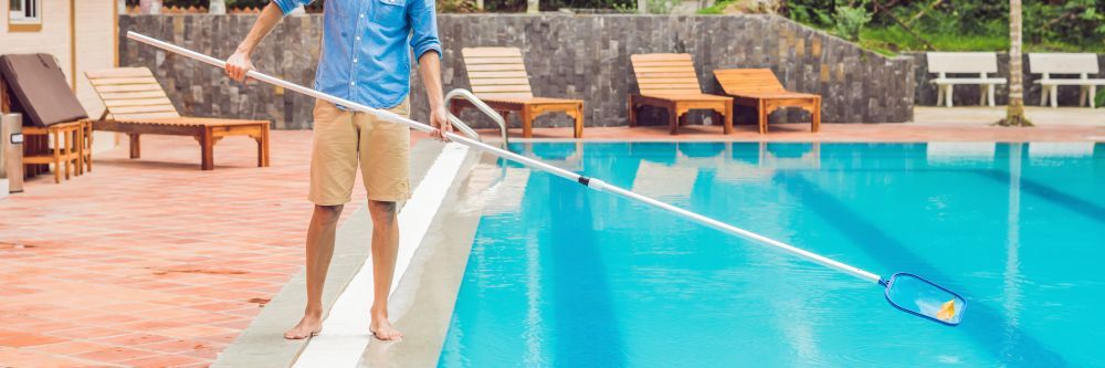 A Man Is Cleaning a Swimming Pool with A Broom —
Whitsunday Pool Service in Cannonvale, QLD 