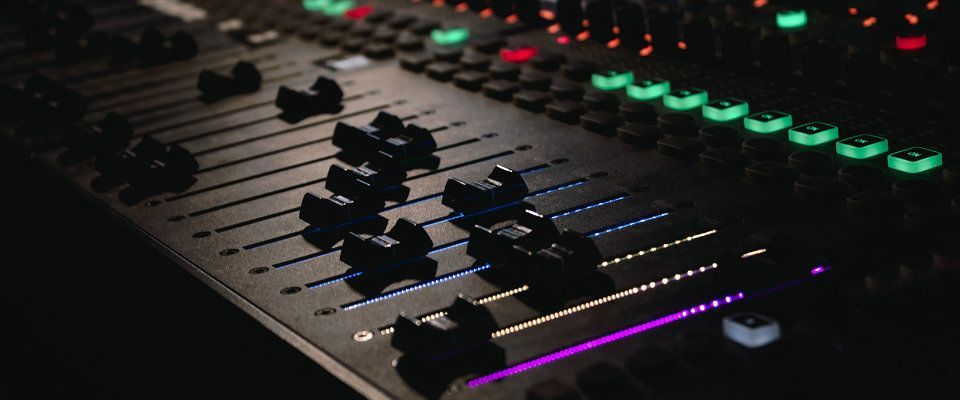 Close-up of an audio mixing console with glowing red, green, and purple LEDs