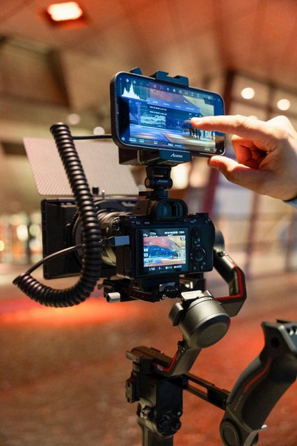 Hand adjusting a smartphone mounted on a camera rig with a monitor and coiled cable
