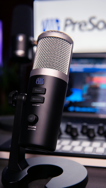 Black podcast microphone on a desk stand in front of a blurred laptop screen