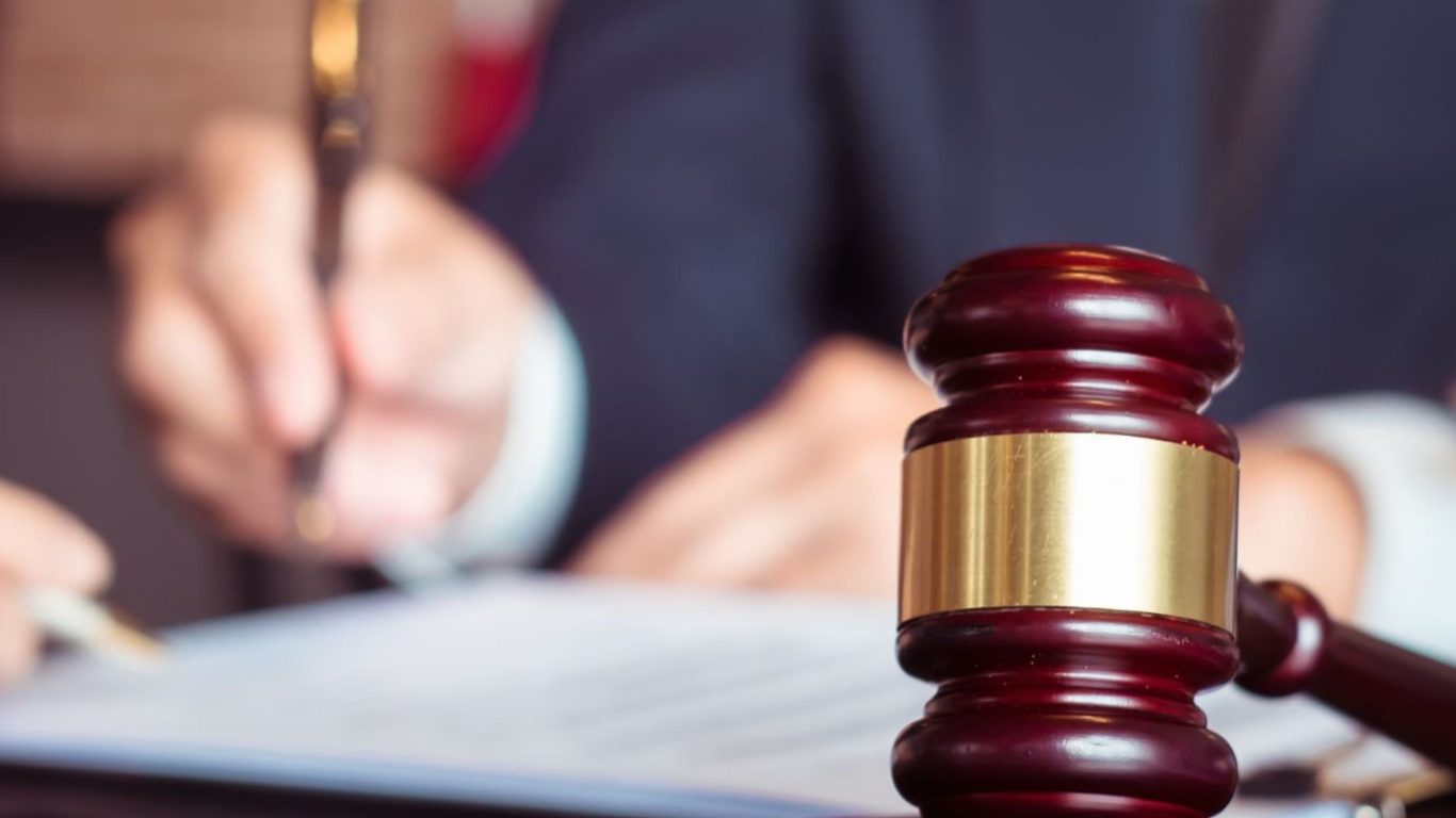 Wooden gavel on a table with a person signing documents in the background.