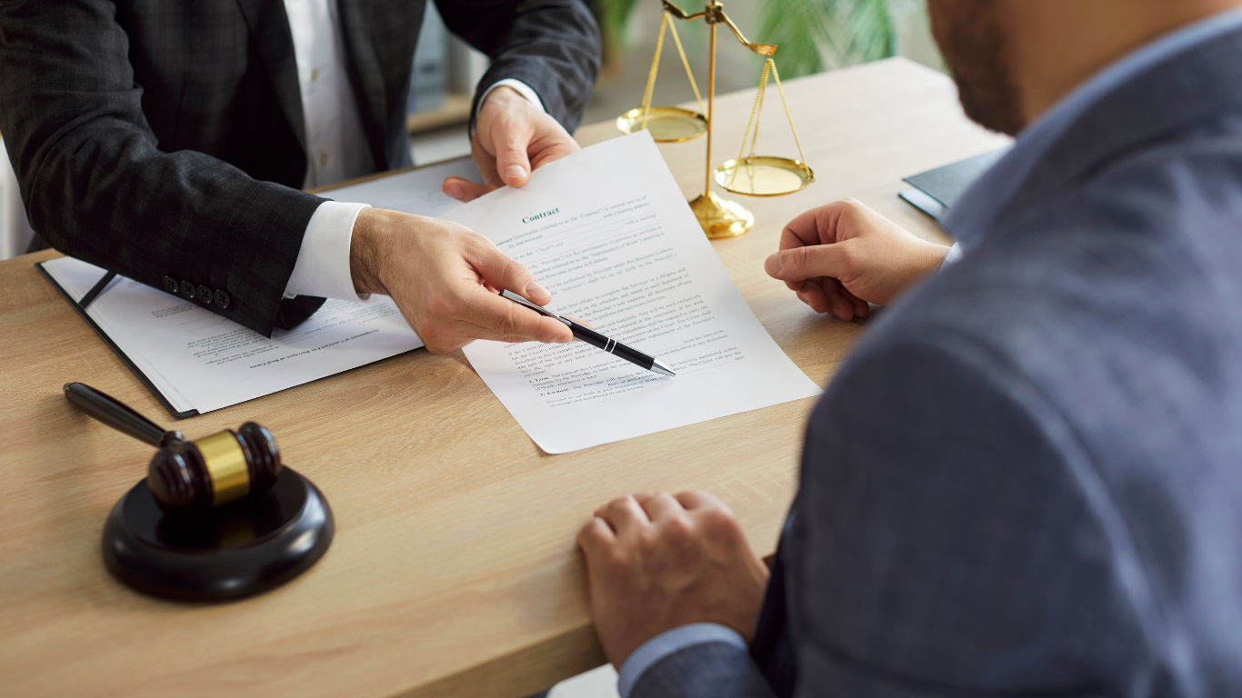 Lawyer signing a contract at a desk with a gavel, law books, and scales of justice in the background.