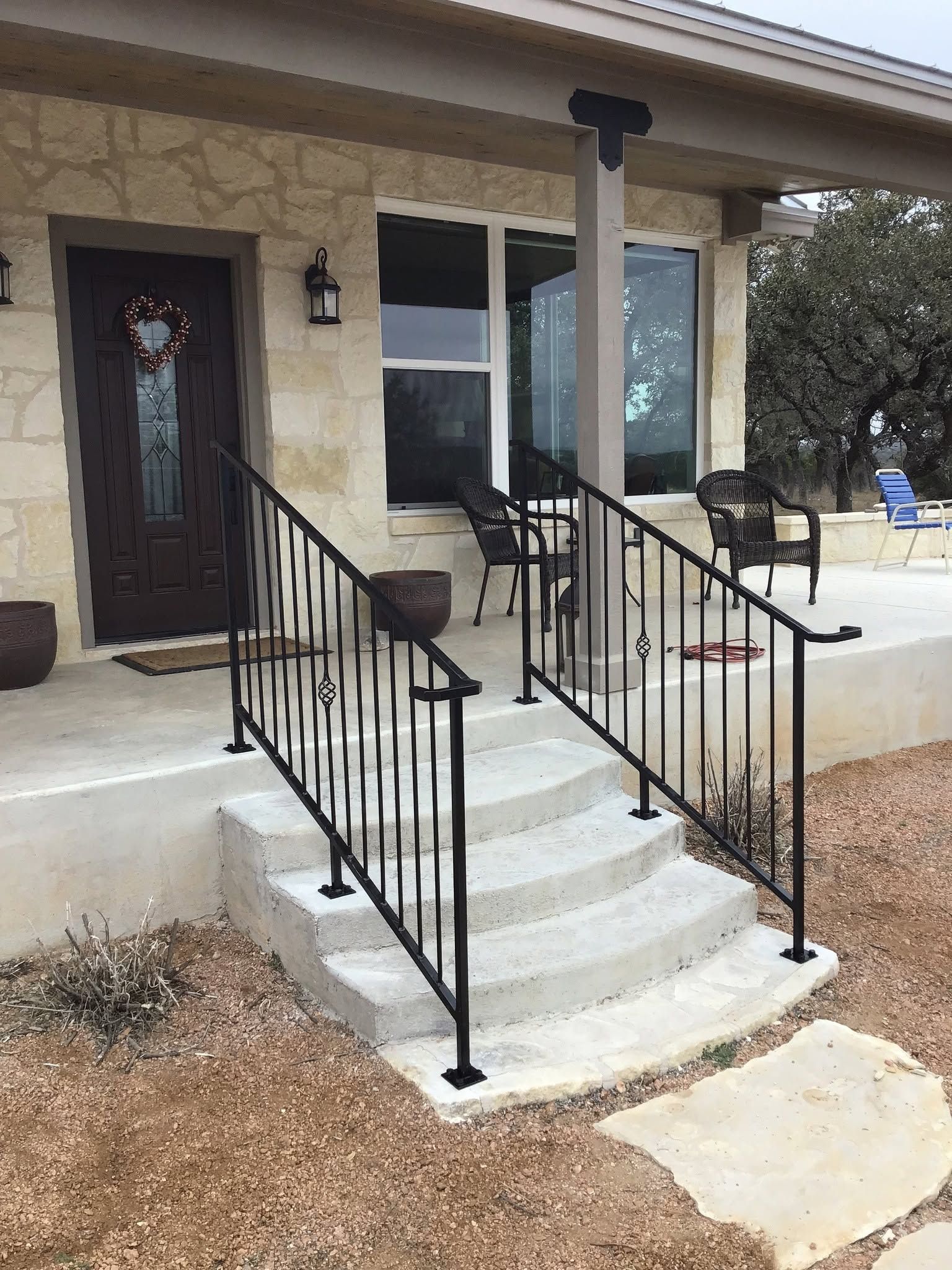 Front porch with concrete steps, black railings, and a dark front door on a beige house.