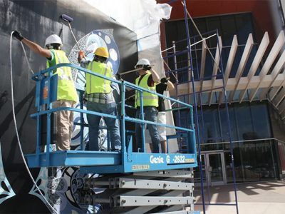 Workers in safety vests on a lift installing exterior panels on a building facade