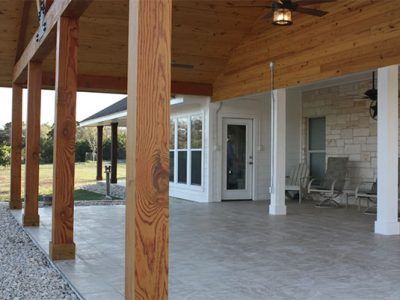 Covered porch with wooden posts, white columns, and a tiled floor beside a house.
