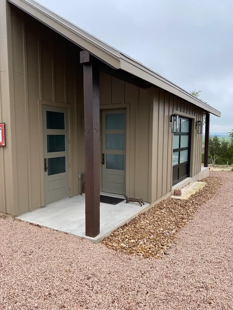 Modern beige building with covered porch, doors and windows, surrounded by gravel under an overcast sky