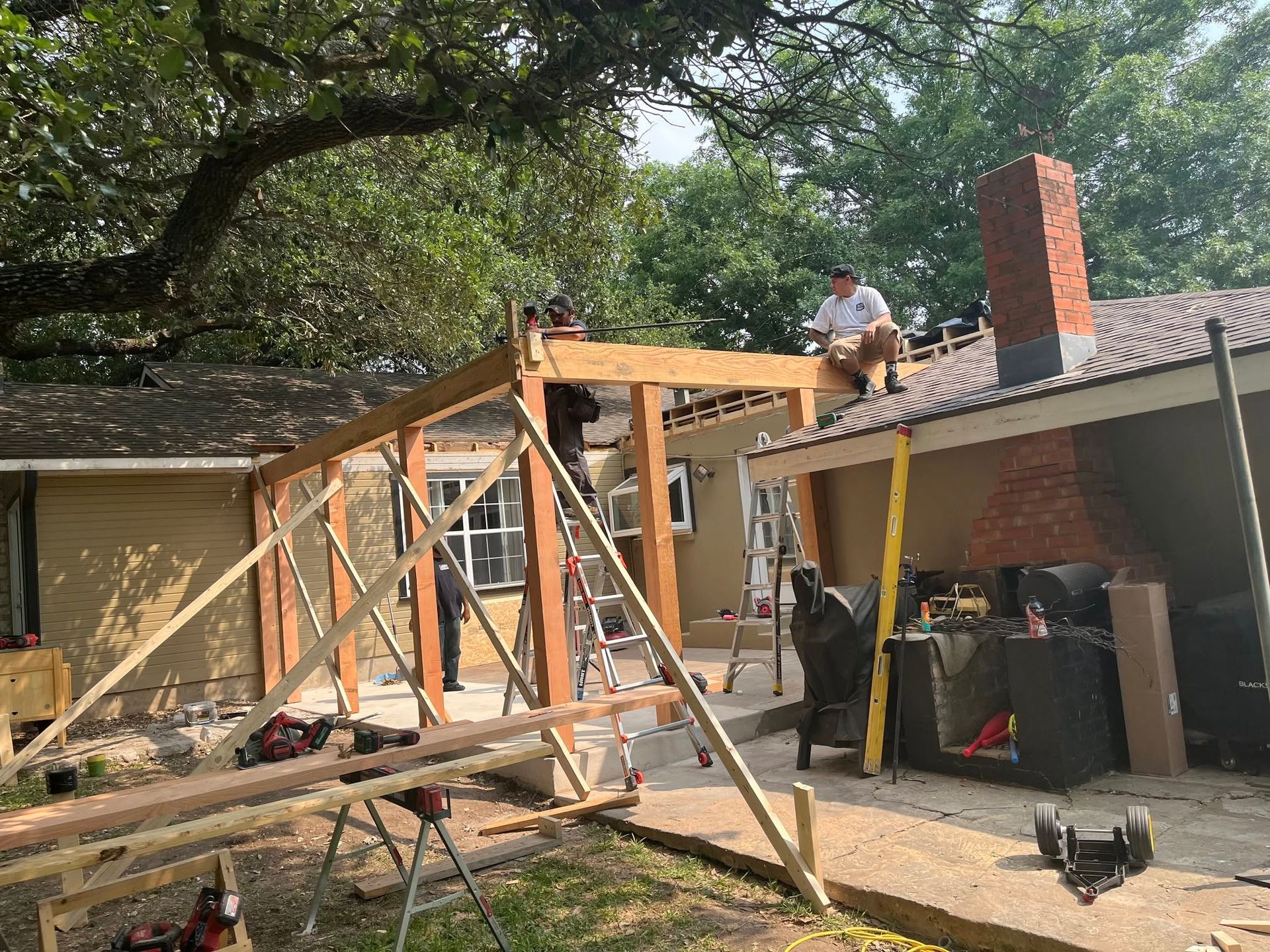 House under construction with wooden framing, debris, and a worker on the roof beside a chimney