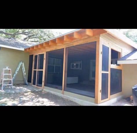Partially constructed patio with wood framing, large open sliding doors, and ladders outside a house