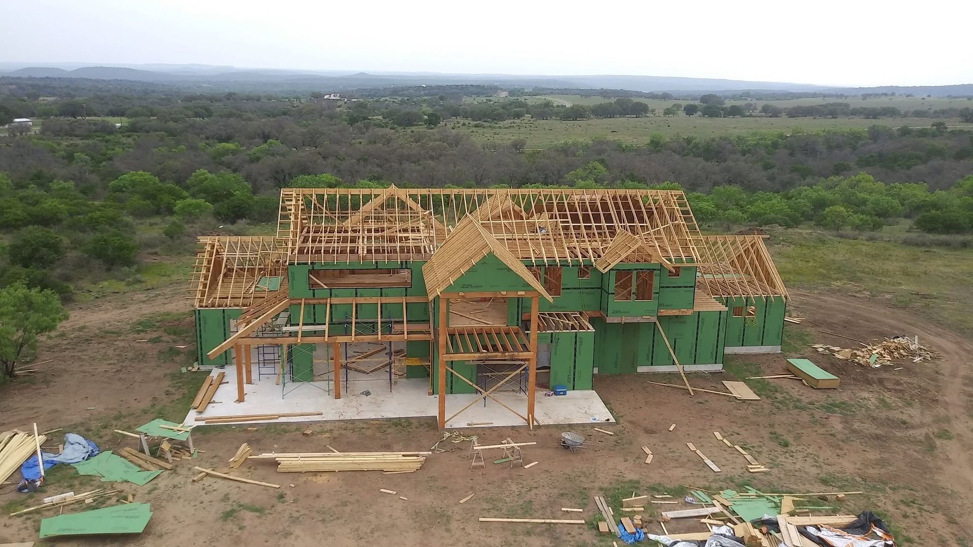 Partially built green house frame in a cleared rural area, with forest stretching into the distance.