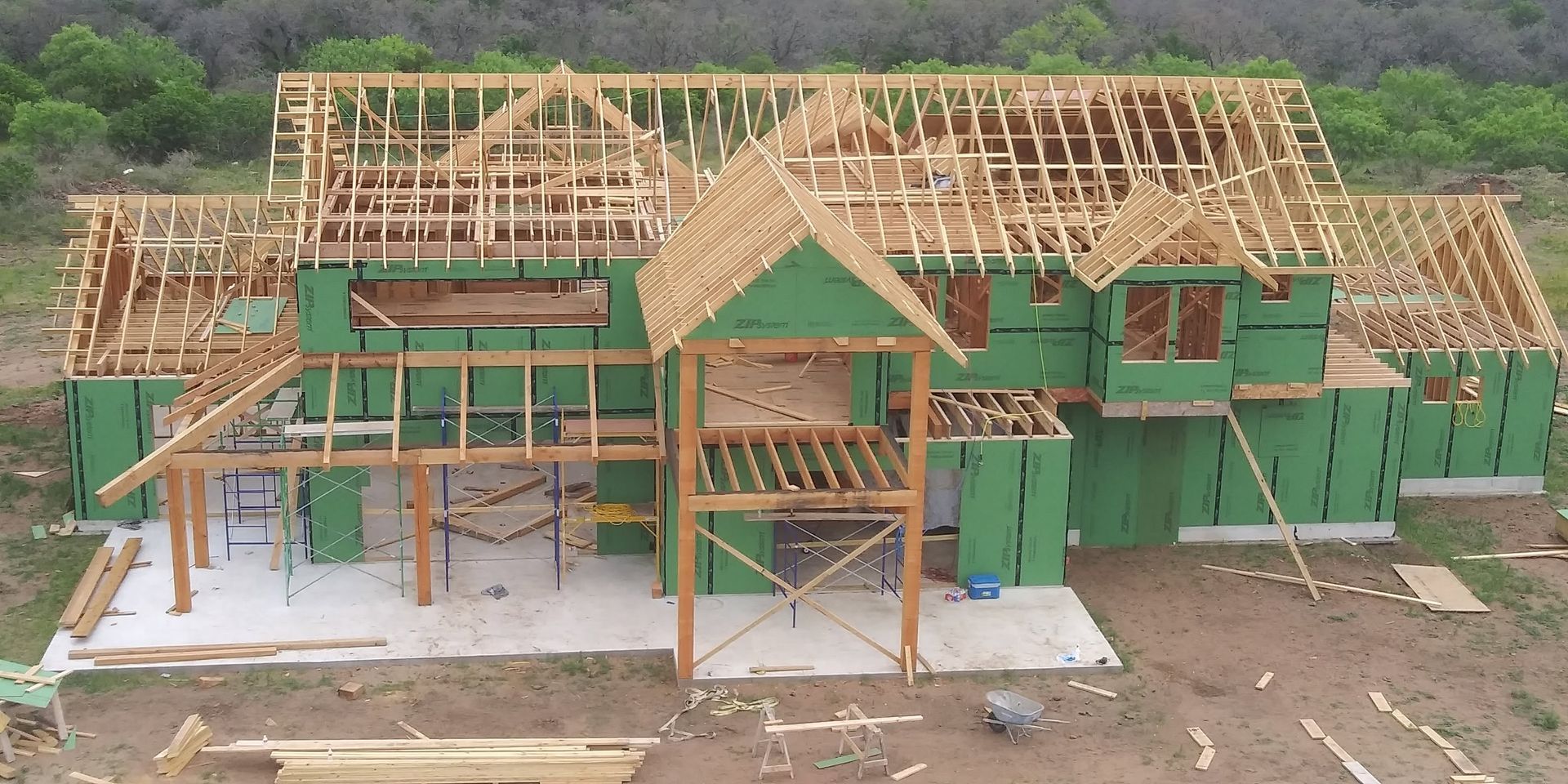 Partially built house with green sheathing and exposed wooden roof framing on a construction site