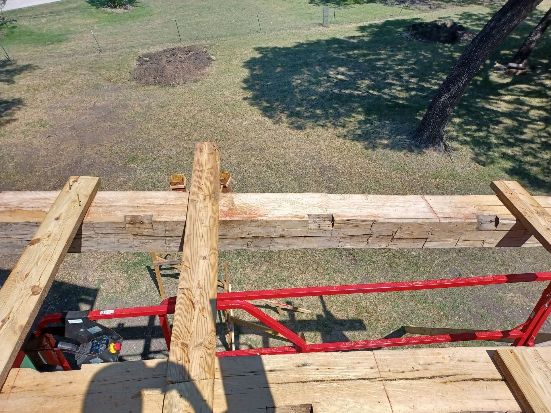 View from a roof with wooden planks and red scaffolding overlooking a grassy yard.