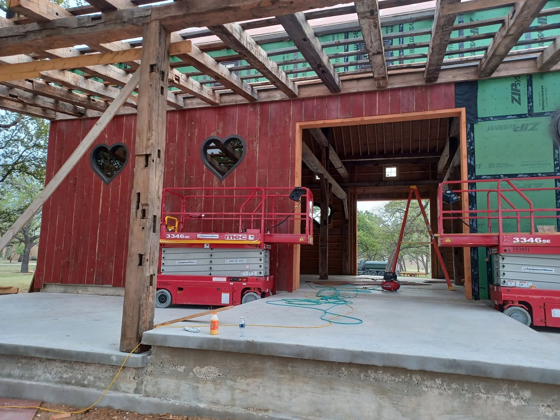 House under construction with exposed wood framing and red lift equipment at the entrance