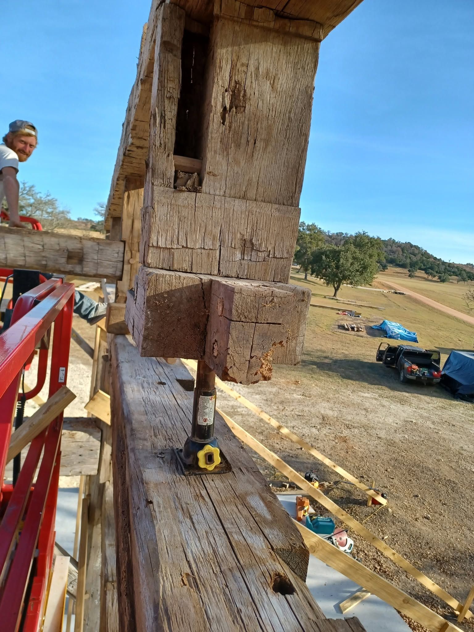A large construction machine crushes a concrete block on a wooden platform in an open outdoor area.