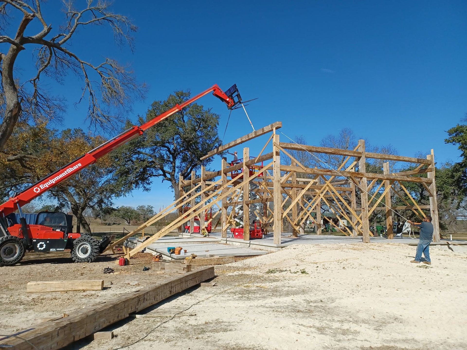 Construction site with wooden frame house, red boom lift, and workers under a clear blue sky