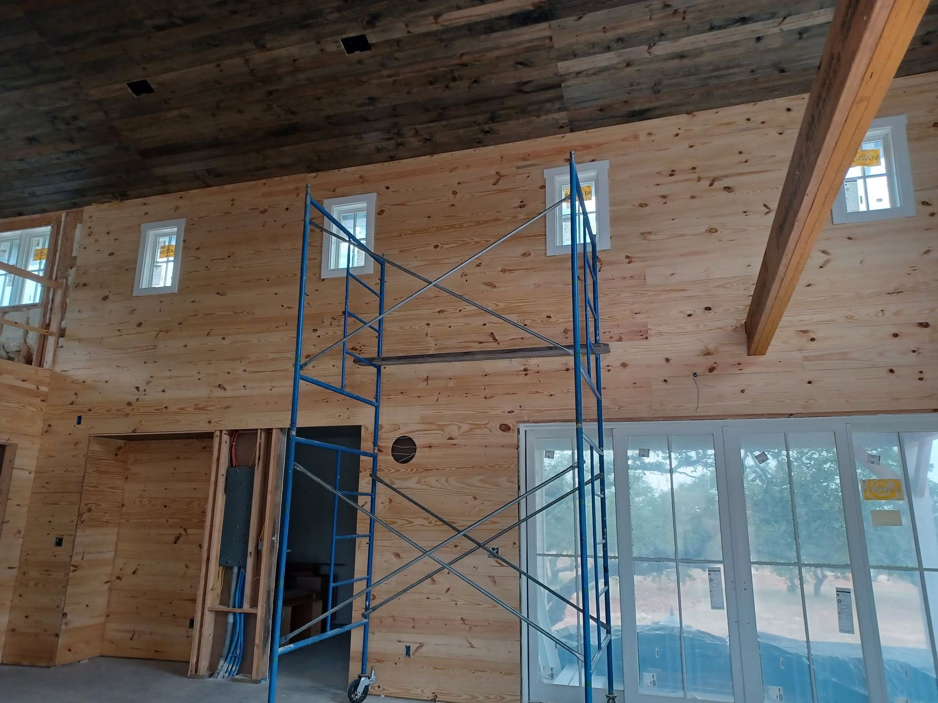 Interior of a wood-paneled room under construction with scaffolding and large windows.