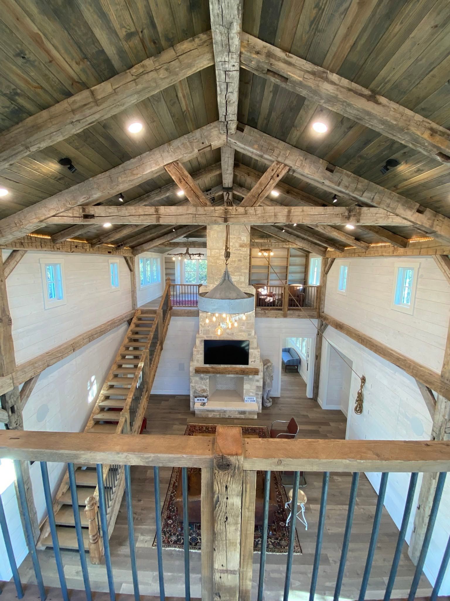 Rustic loft interior with exposed beams, central stone fireplace, and staircases on both sides