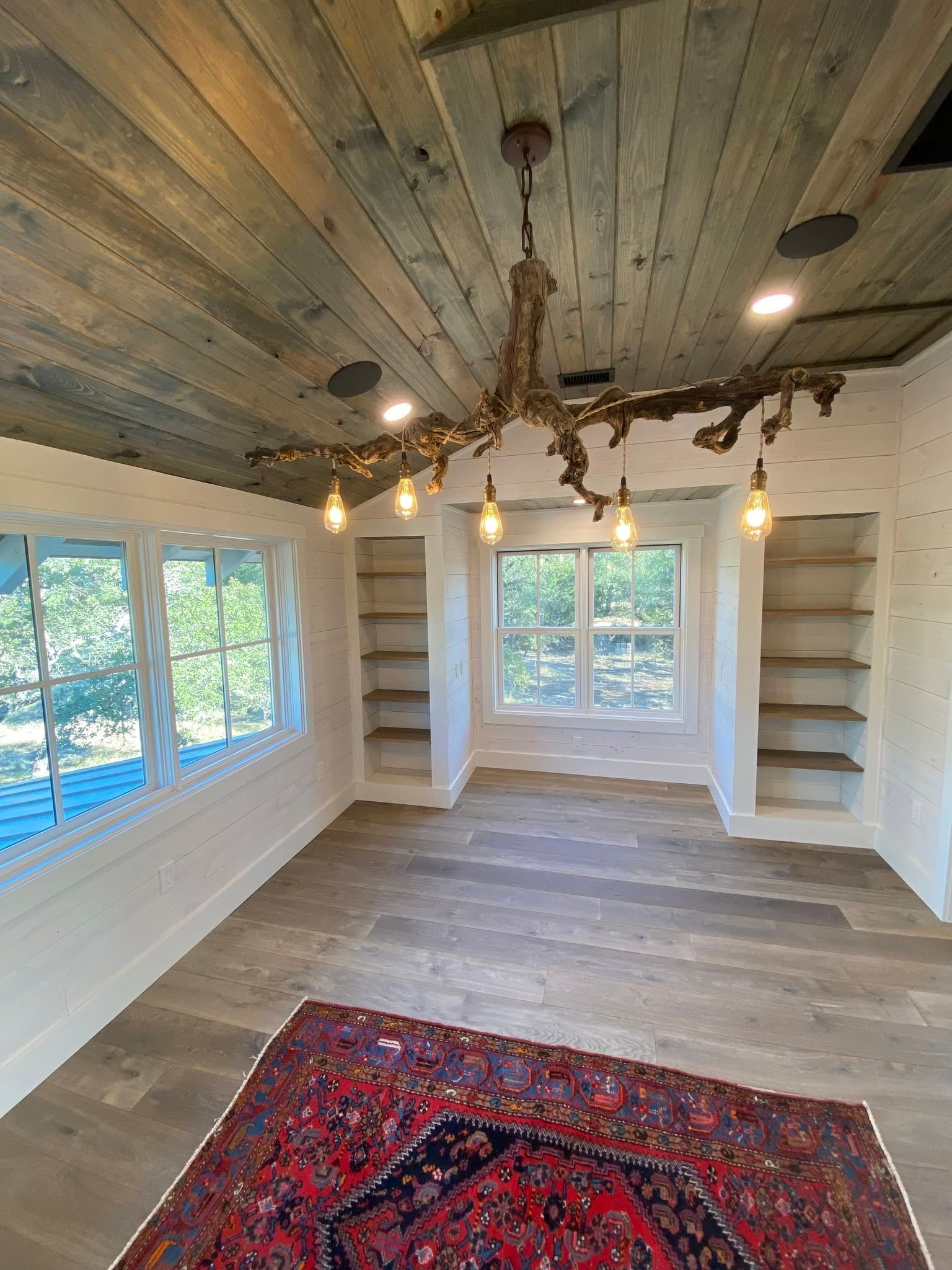 Small empty room with wood ceiling, white walls, windows, hanging lights, and red rug.
