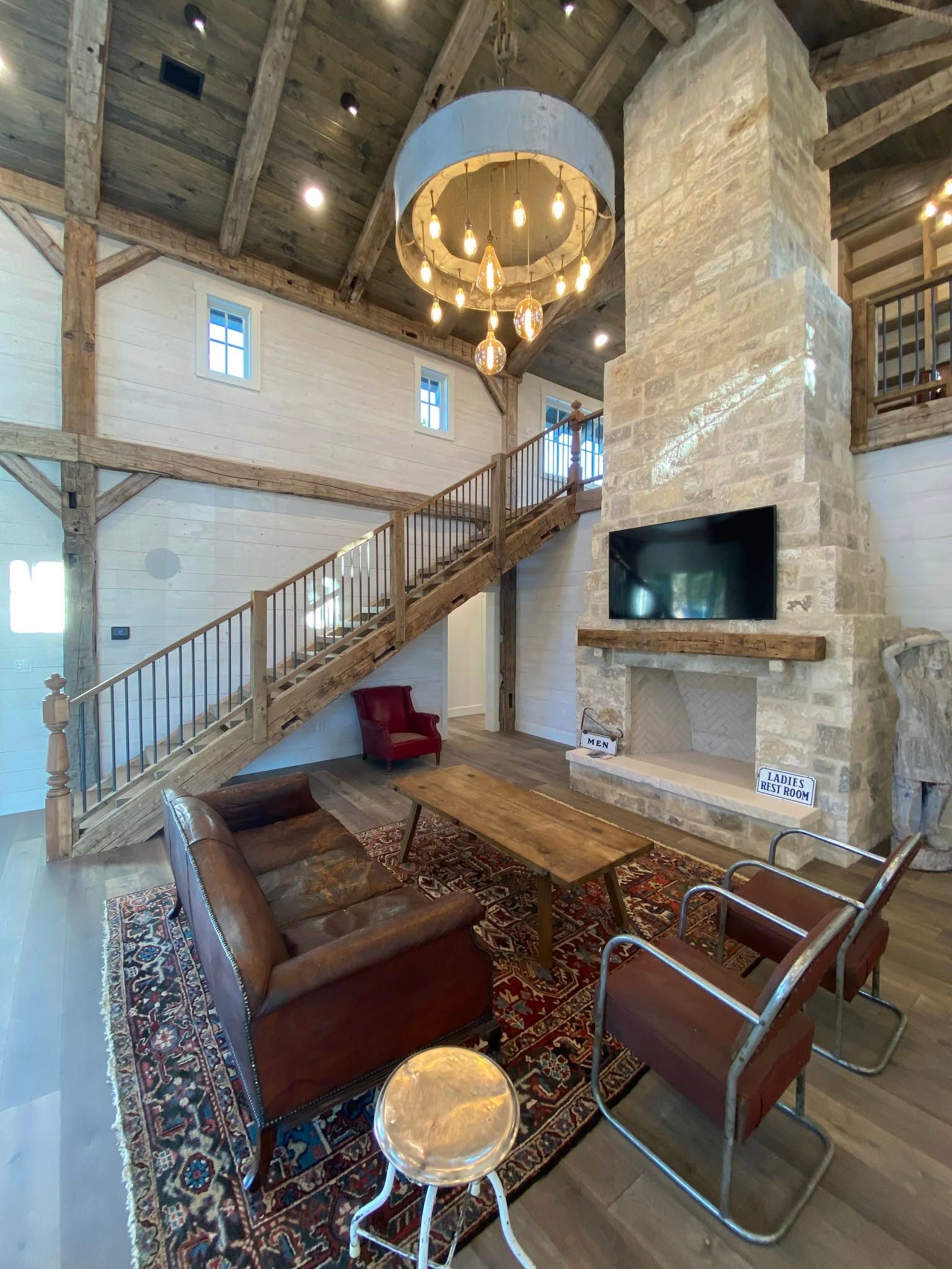 Rustic stone living room with leather sofas, staircase, chandelier, and wall-mounted TV