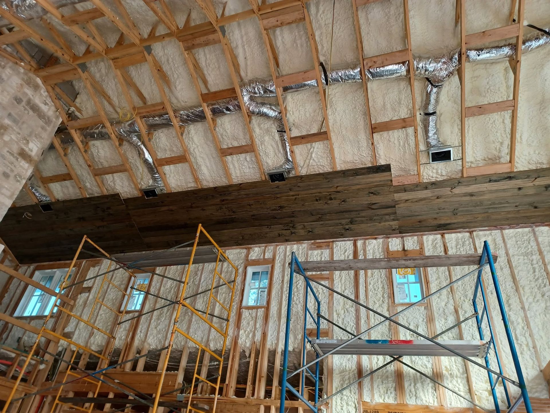 Scaffolded interior under construction with insulated ceiling and exposed wooden beams.
