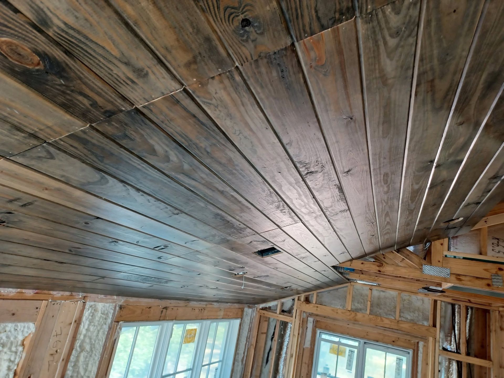 Wooden ceiling with weathered planks and exposed beams above windows in a rustic room