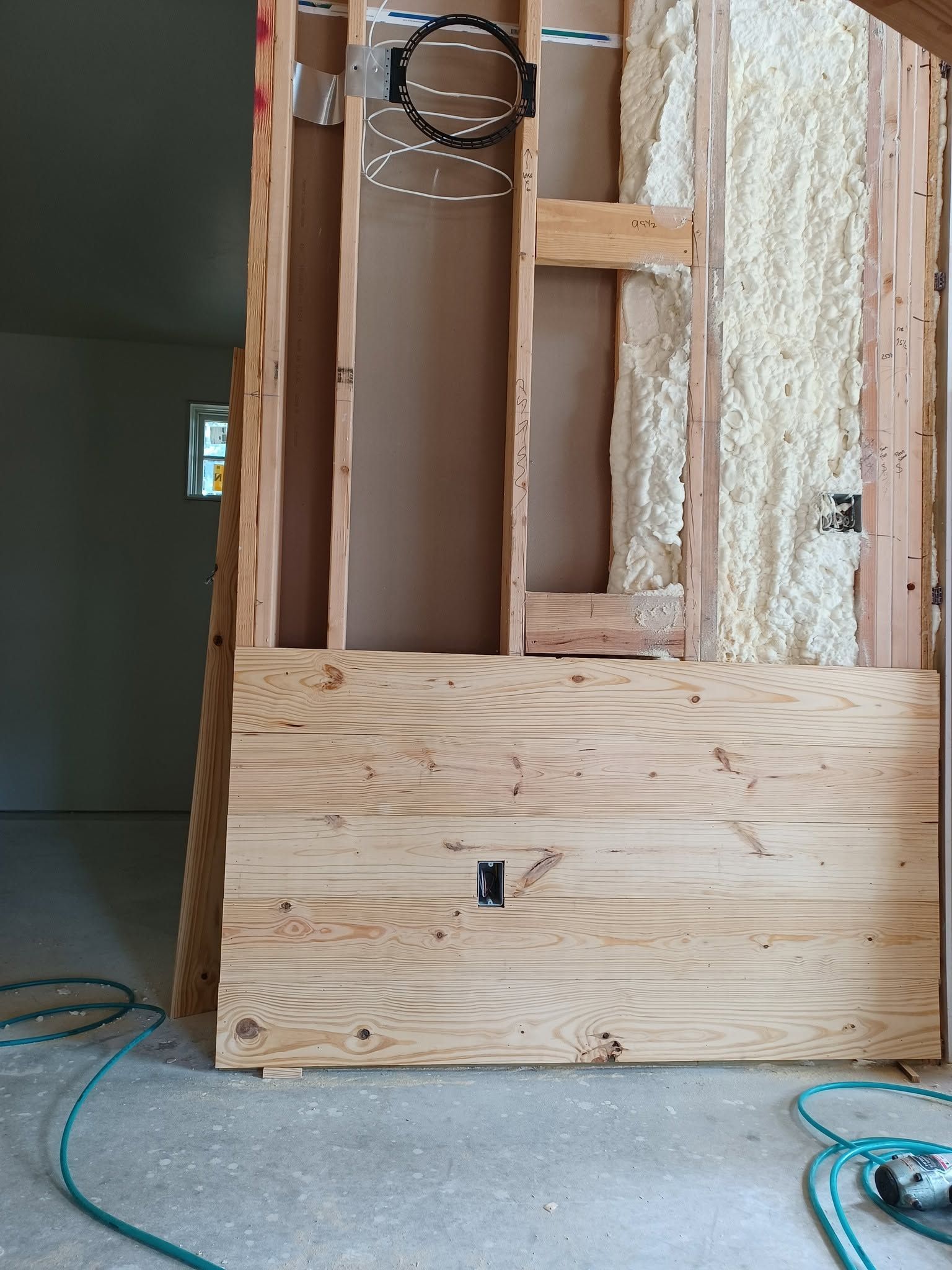 Partially framed wall with exposed studs, wiring, and plywood sheathing in an unfinished room.