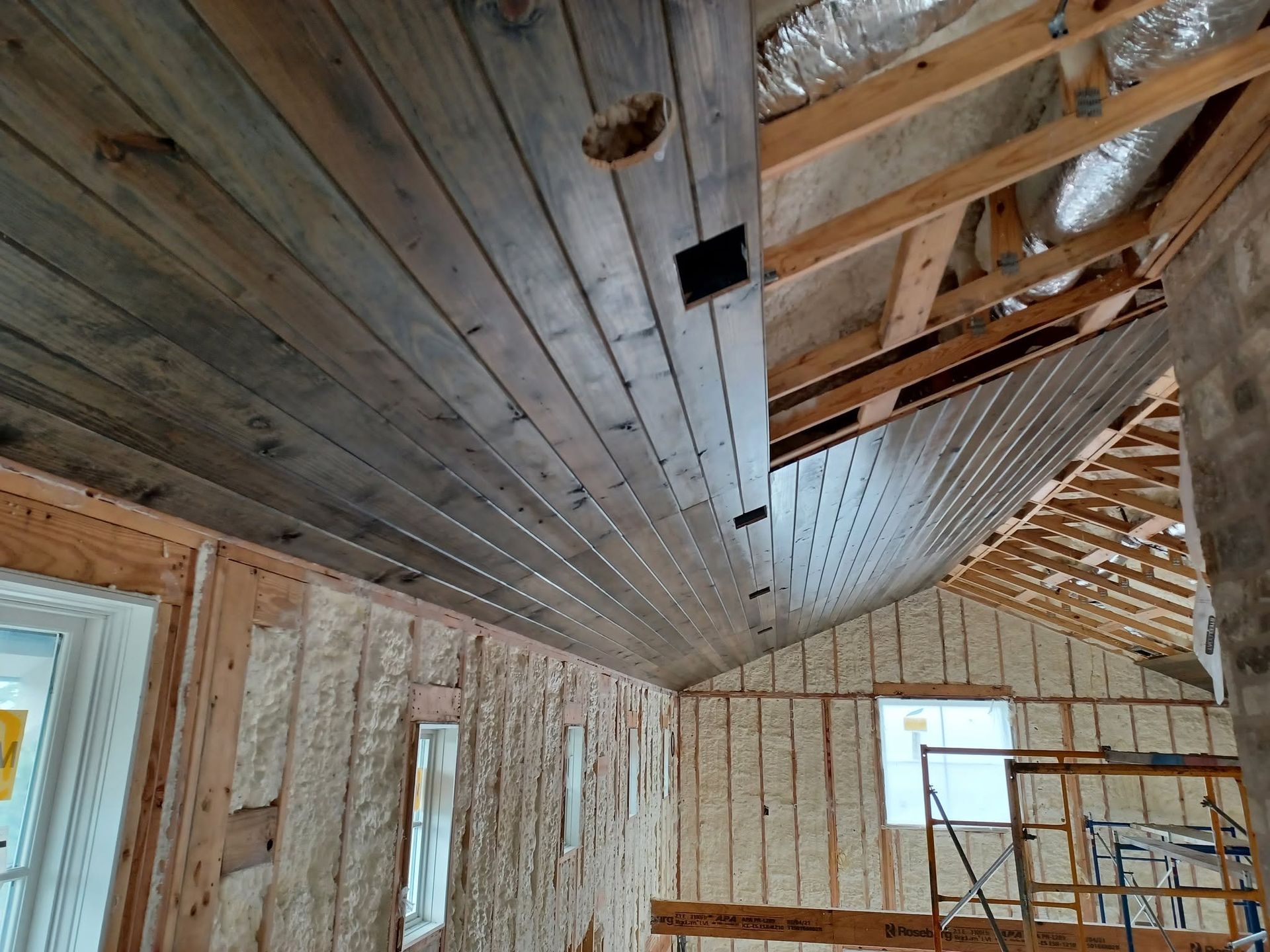 Interior of a house under renovation, with exposed wood framing and unfinished ceiling beams.