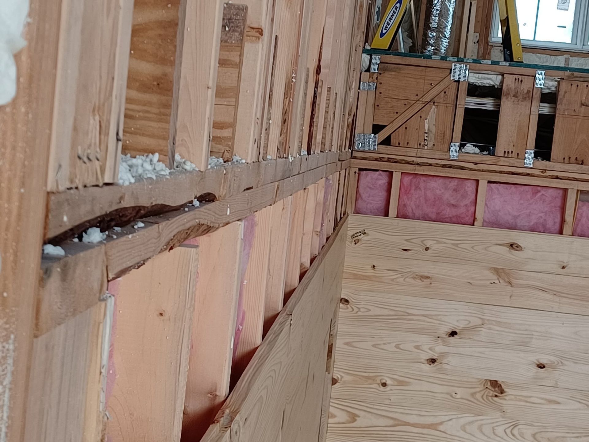 Interior of a house under construction with exposed wooden framing and pink insulation panels