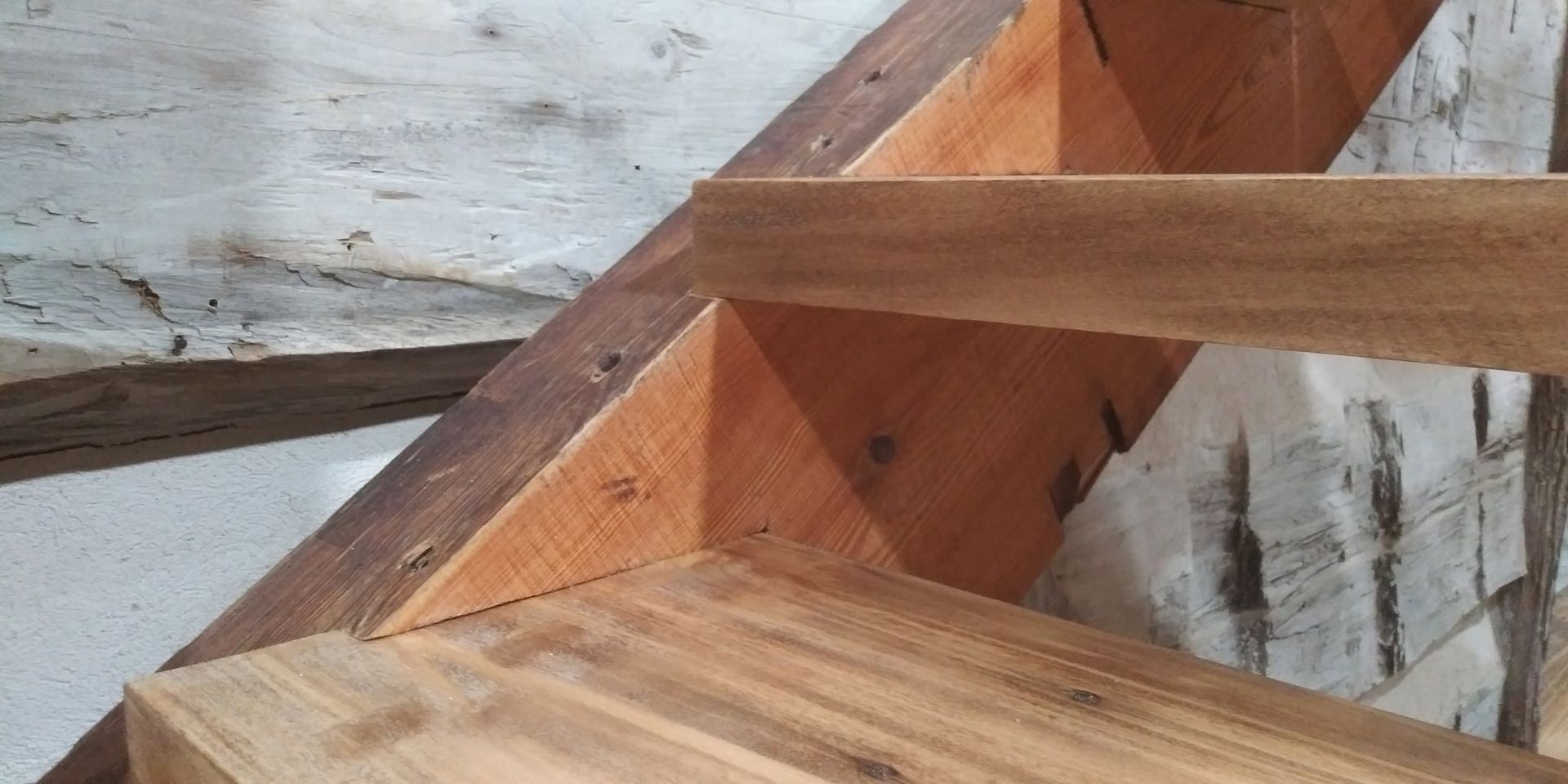Close-up of wooden stair framing and diagonal support beams against a rough wall.