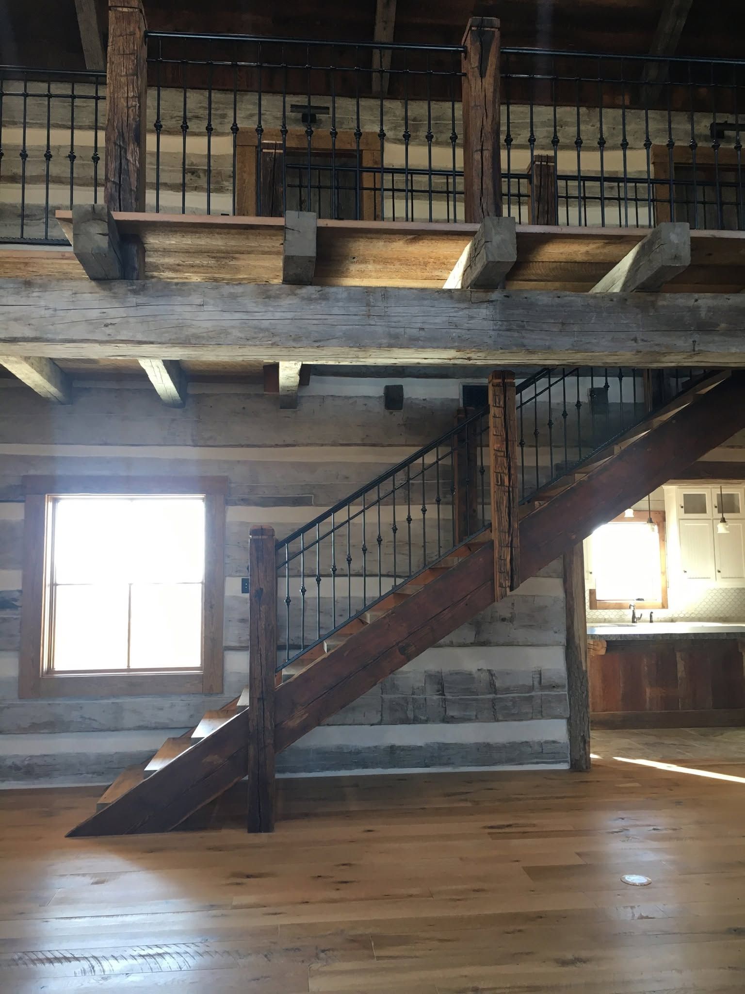 Rustic loft interior with exposed beams, wooden staircase, and large windows over wood floors
