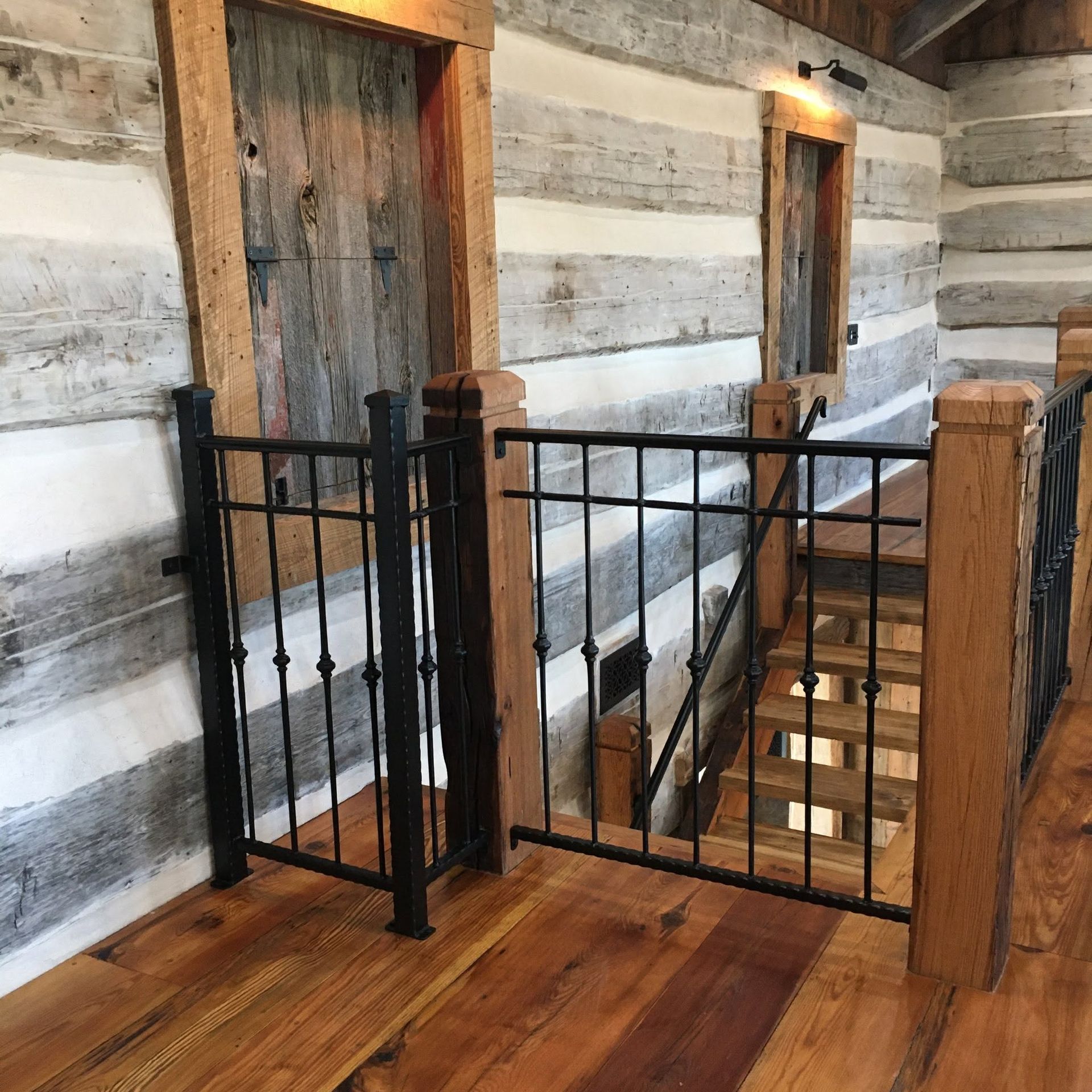 Rustic cabin interior with wooden floors, log walls, and a black metal stair gate by a staircase opening