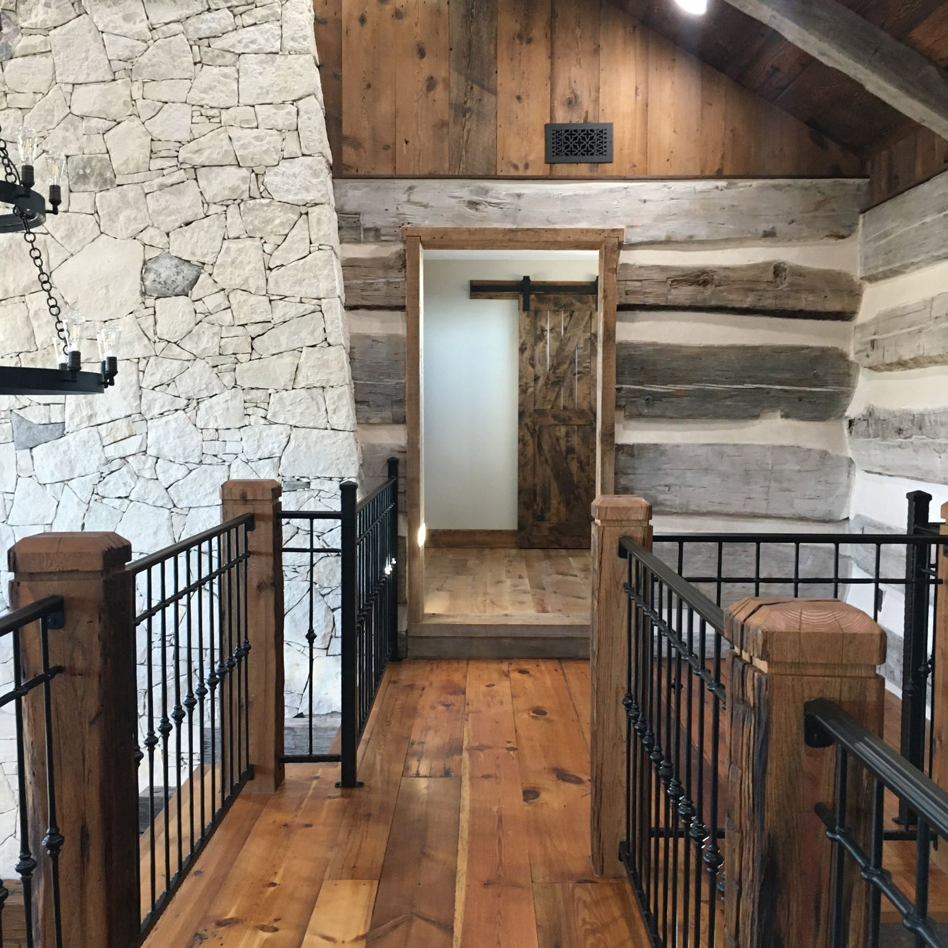 Rustic wooden hallway with black railings leading to a narrow doorway in a log cabin interior